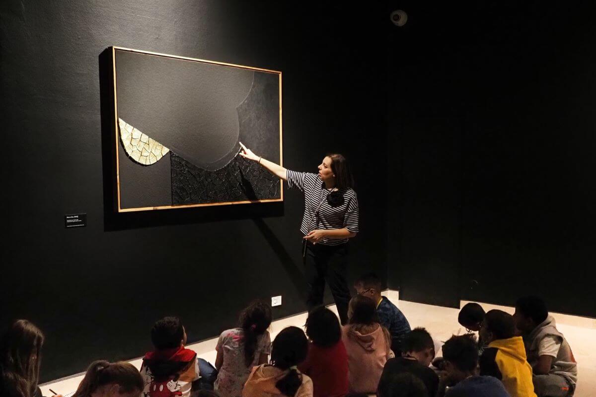 Un momento della visita guidata alla mostra di Burri con alcuni bimbi seduti per terra che guardano la guida