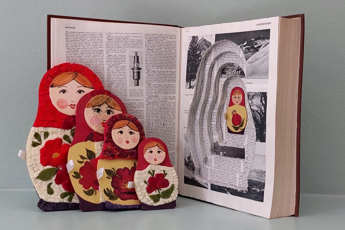 Immagine di un libro aperto con dentro una piccola matrioska e mosaico, altre quattro accanto.