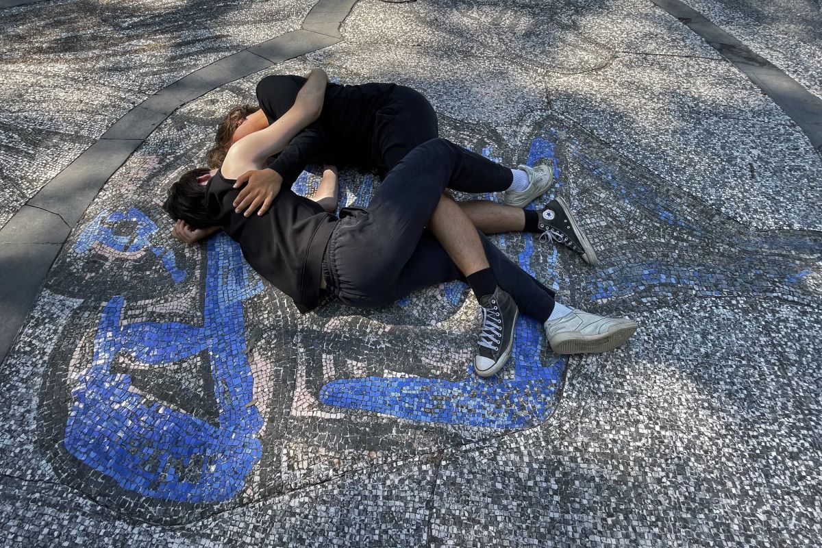 Immagine di due persone a terra sul mosaico di Mimmo Paladino al Parco della Pace.