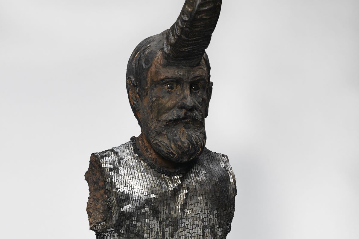 Dettaglio di una scultura musiva col busto di un uomo e un grande corno al centro della fronte.