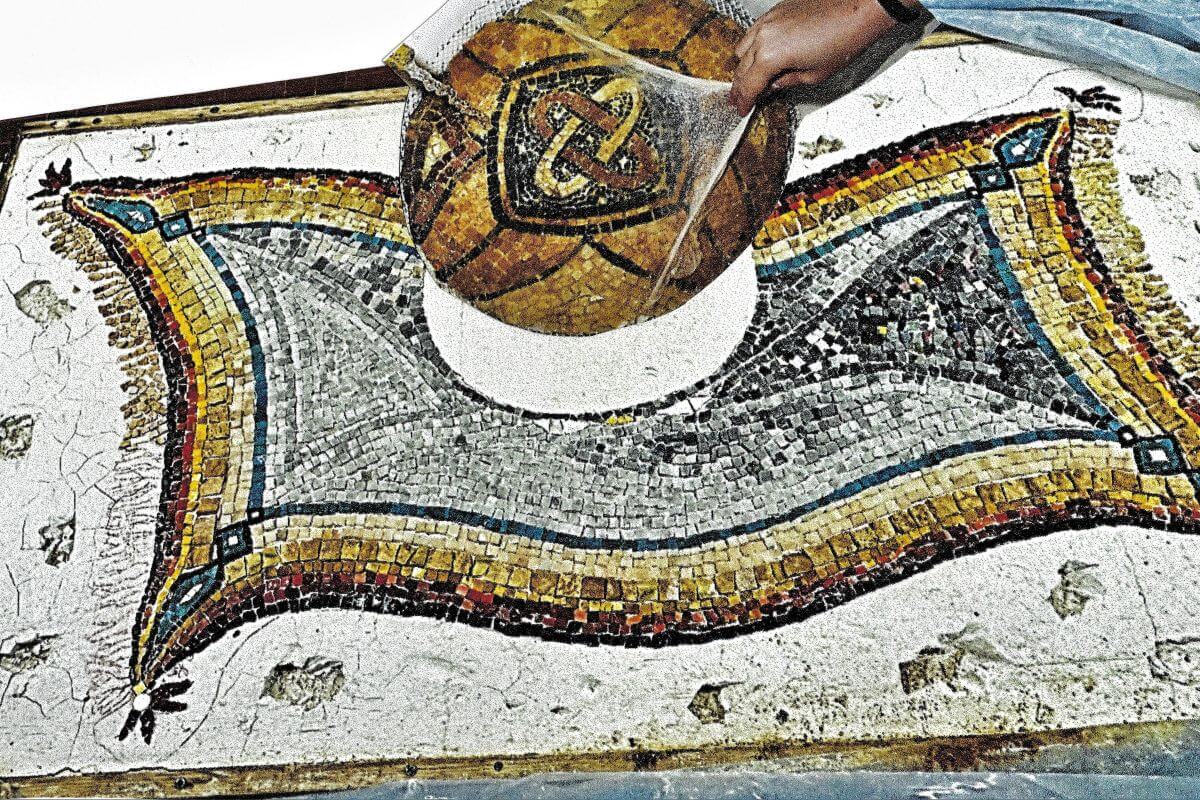 Foto di un mosaico in cui un elemento circolare viene posato da una mano.