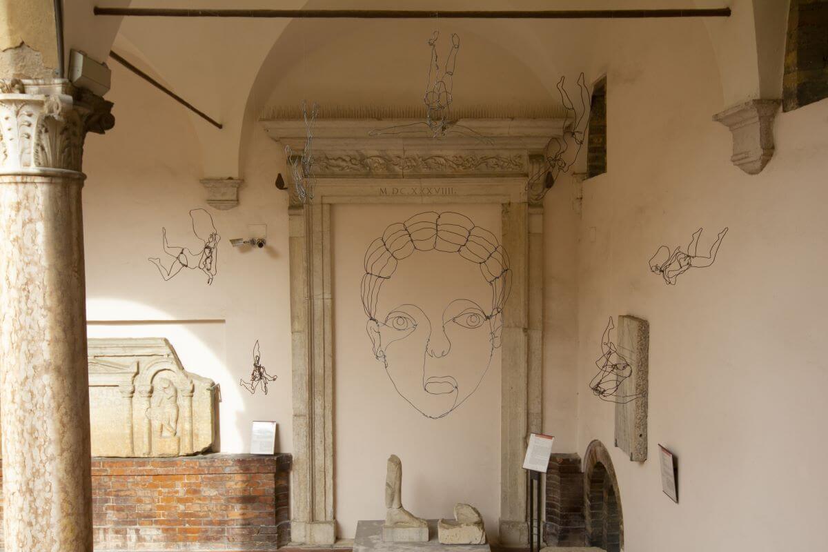 Foto di una parte del chiostro con opere in marmo e installazioni in ferra con visi umani e piccole figure umane.